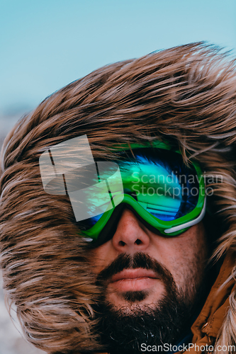 Image of Headshot photo of a man in a cold snowy area wearing a thick brown winter jacket, snow goggles and gloves. Life in cold regions of the country.