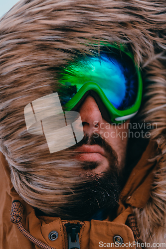 Image of Headshot photo of a man in a cold snowy area wearing a thick brown winter jacket, snow goggles and gloves. Life in cold regions of the country.