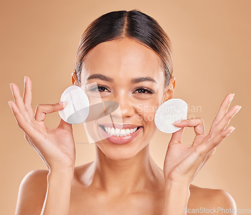 Image of Face, dermatology and woman with cotton pad, organic facial and smile against a brown studio background. Portrait, female or lady with skincare, makeup remover and happiness with glow and smooth skin