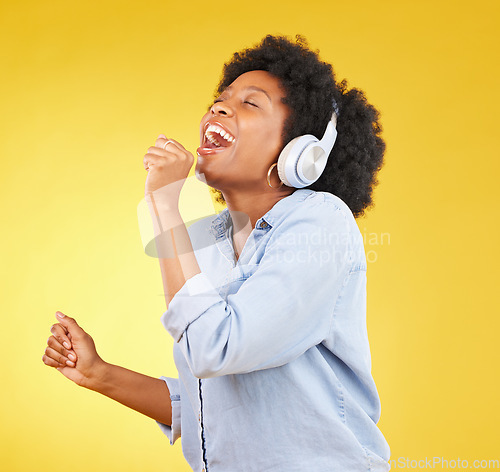 Image of Black woman, singing with headphones and freedom, music and happiness with invisible mic on yellow studio background. Happy female, carefree and radio, audio streaming, fun and energy with technology