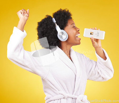 Image of Black woman, music headphones and singing with phone in studio isolated on a yellow background. Karaoke singer, bathrobe and happy female dance with mobile microphone while streaming podcast or radio