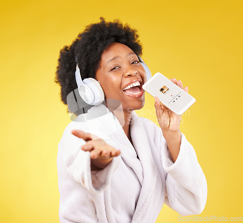 Image of Black woman, music headphones and singing with phone in studio isolated on a yellow background. Karaoke singer, bathrobe and face portrait of happy female with mobile while streaming podcast or radio