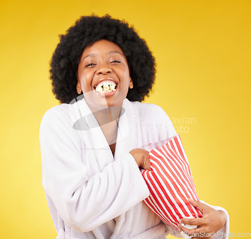 Image of Funny face, portrait and black woman eating popcorn in studio isolated on a yellow background. Comic smile, food and laughing, hungry and happy female eat corn or snack in morning gown or bathrobe.