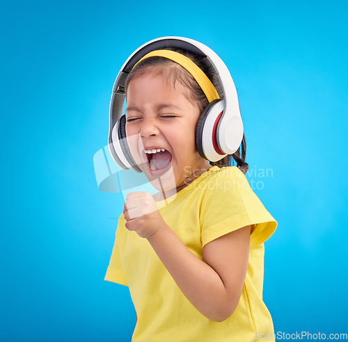 Image of Music, headphones and singing with girl in studio for streaming, mobile radio and audio. Technology, media and youth with child listening isolated on blue background for natural, happy and songs