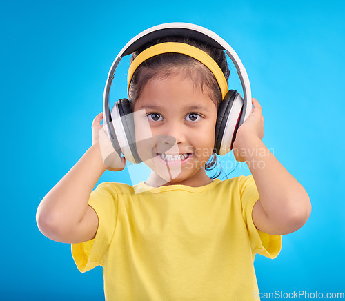 Image of Music, headphones and listening with portrait of girl in studio for streaming, mobile radio and audio. Technology, media and youth with child isolated on blue background for natural, happy and songs