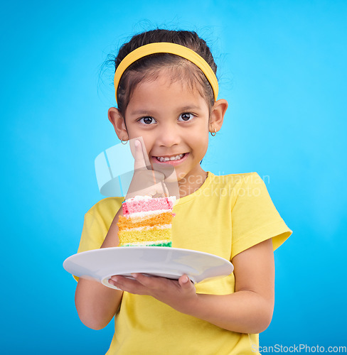 Image of Birthday cake, portrait and young girl with sweet in studio eating icing for party event dessert. Celebration, rainbow food and hungry kid in a isolated and blue background youth ready to celebrate