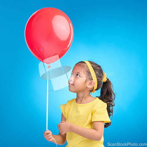 Image of Young girl, studio and red balloon of a an kid alone ready for a birthday party to celebrate. Celebration event and female child holding balloons in the air with isolated blue background