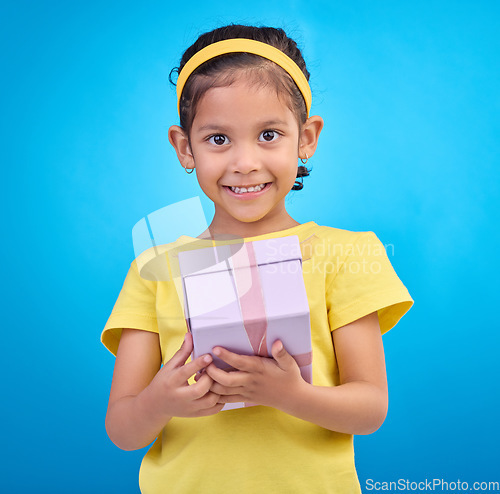 Image of Gift, box and smile with portrait of girl in studio for celebration, shopping and birthday event. Happiness, surprise and present with child for party, giveaway or product isolated on blue background