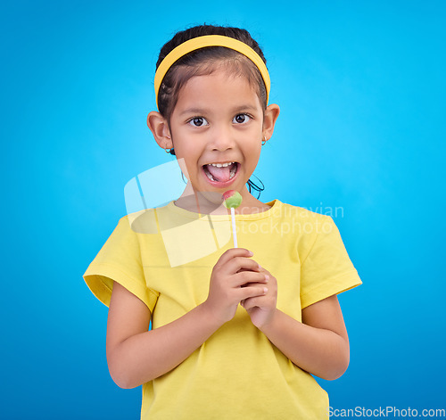 Image of Young girl, portrait and lollipop with a student feeling happy with a smile and blue background. Isolated, cute and adorable child face with happiness, joy and cheerful from dessert and sweet