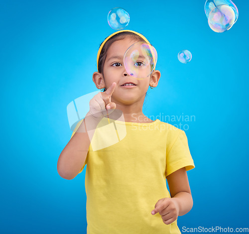 Image of Children, cute and a girl popping bubbles on a blue background in studio for fun or child development. Kids, motor skills and pointing with a female youth playing a game alone on a color wall