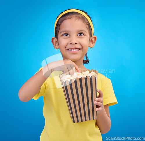 Image of Popcorn, eating and watching movie with girl in studio for food, cinema and comedy. Laugh, television and film with child and snack for streaming, subscription and tv isolated on blue background