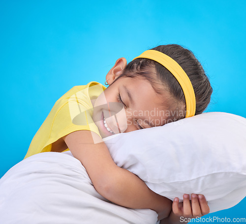 Image of Young girl smile, pillow and sleep in a studio feeling tired, fatigue and ready for dreaming. Isolated, blue background and happy little child with pillows and closed eyes for sleeping, rest and nap