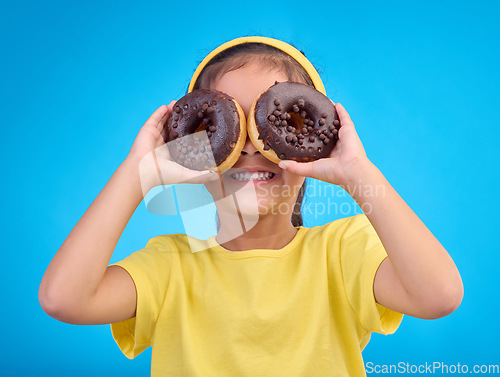 Image of Donut, eyes and covering face of playful cute girl with food isolated against a studio blue background with a smile. Adorable, happy and young child or kid excited for sweet sugar doughnuts