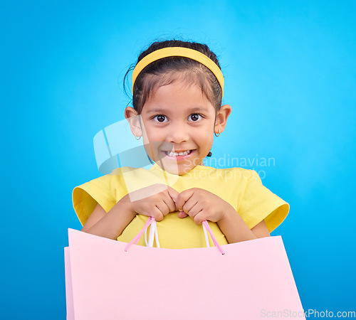 Image of Girl smile, portrait and gift bags from birthday party, event or celebration with a present in studio. Shop choice, bag and little child looking at presents with isolated and blue background with kid