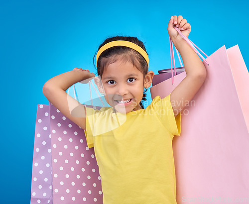 Image of Girl, shopping portrait and gift bags from birthday party, event or celebration with a present in studio. Shop sale, bag and little child with presents with isolated and blue background with a kid