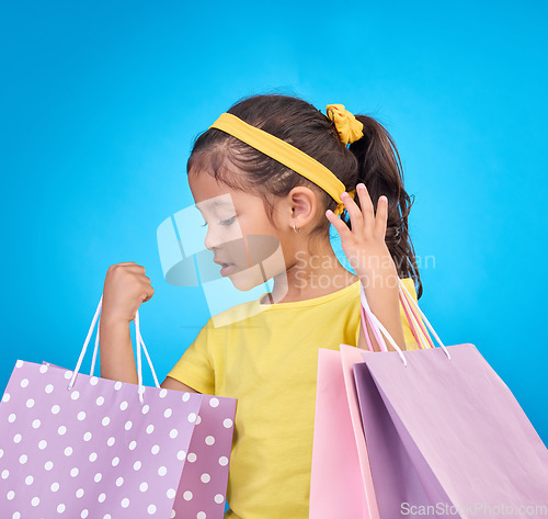 Image of Girl, shopping and gift bags from birthday party, event or celebration with a present in a studio. Shop choice, bag and little child looking at presents with isolated and blue background with a kid