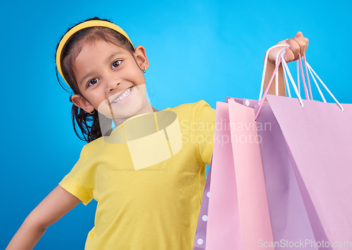Image of Girl portrait, shopping and gift bags from birthday party, event or celebration with a present in studio. Shop, bag and happy child looking at presents with isolated and blue background with a kid