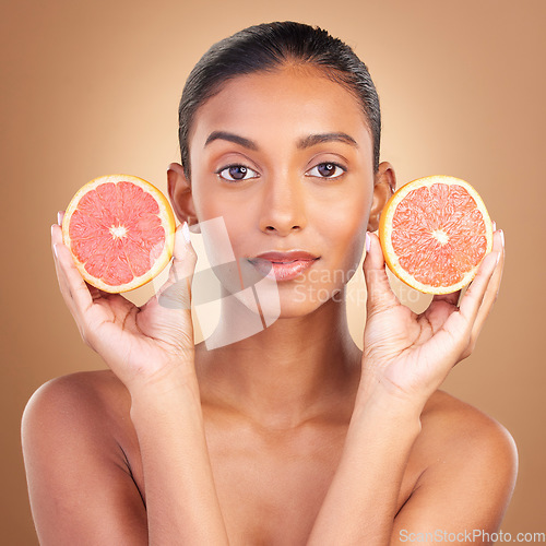 Image of Indian woman, grapefruit and studio portrait for beauty, health or wellness with fruit by brown background. Asian young model and girl with organic citrus fruits for health, cosmetic and skin glow