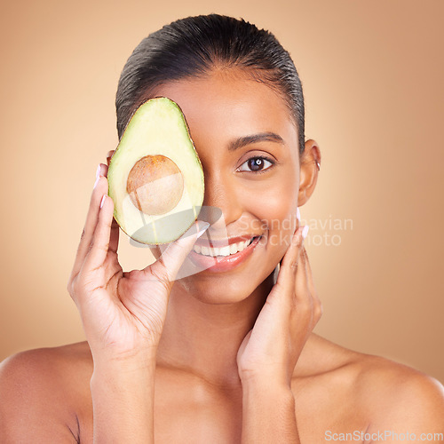 Image of Portrait, skincare and avocado with a woman in studio on a brown background for natural treatment. Face, food or antioxidants with an attractive young female model holding healthy fruit for nutrition