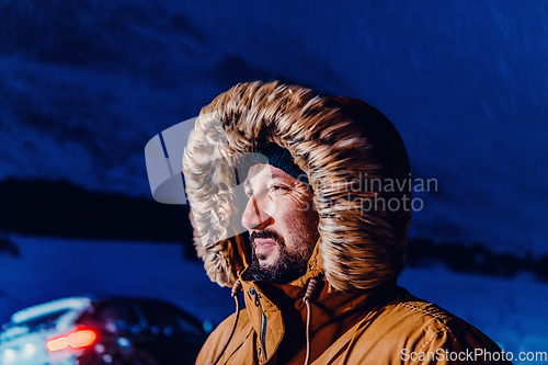 Image of Head shot of a man in a cold snowy area wearing a thick brown winter jacket, snow goggles and gloves on a cold Scandinavian night. Life in the cold regions of the country.