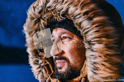 Image of Head shot of a man in a cold snowy area wearing a thick brown winter jacket, snow goggles and gloves on a cold Scandinavian night. Life in the cold regions of the country.
