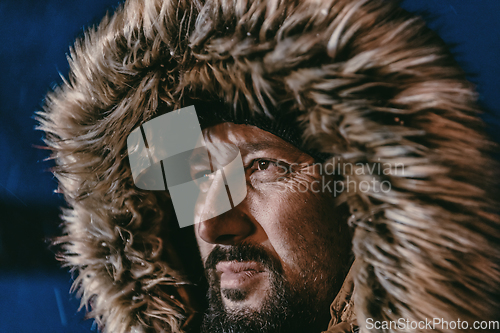 Image of Head shot of a man in a cold snowy area wearing a thick brown winter jacket, snow goggles and gloves on a cold Scandinavian night. Life in the cold regions of the country.