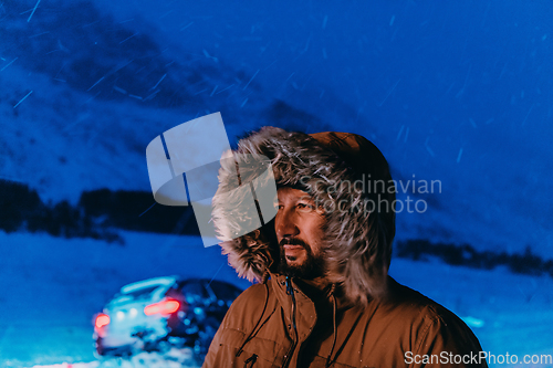 Image of Head shot of a man in a cold snowy area wearing a thick brown winter jacket, snow goggles and gloves on a cold Scandinavian night. Life in the cold regions of the country.