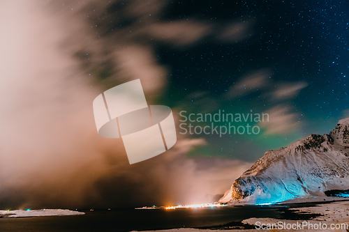 Image of Amazing display of northern lights seen in the north with a bright green band dancing across the sky with a stunning log cabin lodge below.