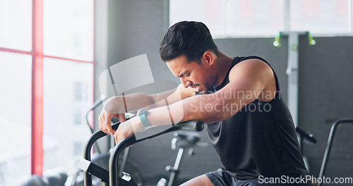 Image of Fitness, bicycle and man tired of cycling for cardio, exercise and training at gym. Wellness, workout and strong Asian man breathing and sweating thinking of motivation and goal on a bike machine