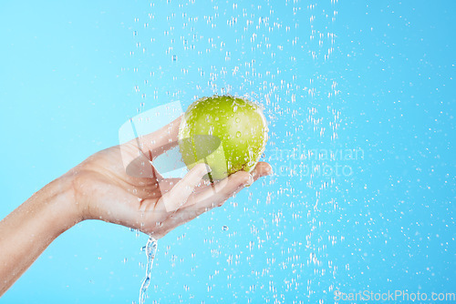 Image of Water drops, apple cleaning and hands with fruit for wellness, healthcare and self care. Healthy food, green and natural skincare with a hand holding health snack for diet in blue background studio