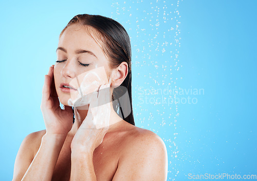 Image of Woman face wash, shower water and studio with a young female doing skincare and beauty routine. Bathroom, dermatology and facial treatment of a model with mock up and isolated blue background