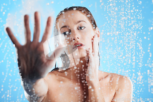 Image of Shower, water drops and woman hand doing skin cleaning, wellness and beauty routine in bathroom. Isolated, blue background and studio with a young female doing hair care and dermatology facial