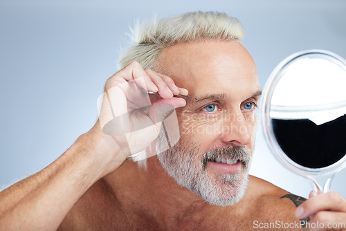 Image of Senior man, tweezers and mirror check in a studio doing hair cleaning and grooming. Wellness, dermatology and beauty routine of a mature male model care with grey background and steel tools for face