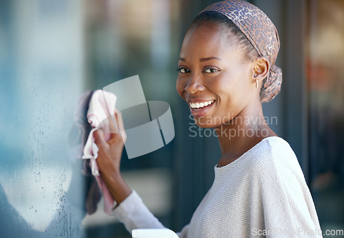 Image of Maid, housekeeper and black woman cleaning and wipe a glass window for hygiene doing housework or chores. Smile, happy and portrait of female cleaner working in a house with detergent to disinfect