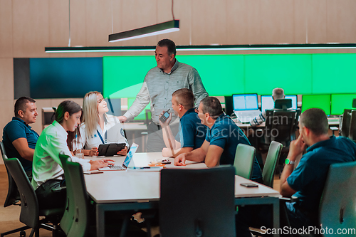 Image of Group of security guards sitting and having briefing In the system control room They're working in security data center surrounded by multiple Screens