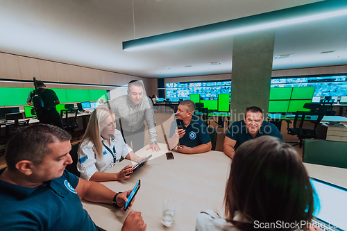 Image of Group of security guards sitting and having briefing In the system control room They're working in security data center surrounded by multiple Screens