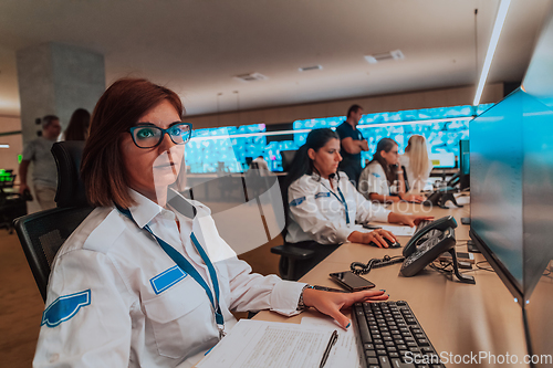 Image of Group of Security data center operators working in a CCTV monitoring room looking on multiple monitors.Officers Monitoring Multiple Screens for Suspicious Activities