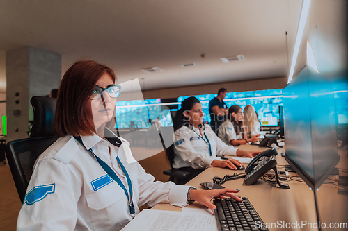 Image of Group of Security data center operators working in a CCTV monitoring room looking on multiple monitors.Officers Monitoring Multiple Screens for Suspicious Activities