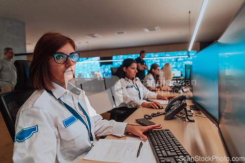 Image of Group of Security data center operators working in a CCTV monitoring room looking on multiple monitors.Officers Monitoring Multiple Screens for Suspicious Activities