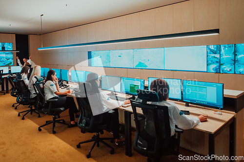 Image of Group of Security data center operators working in a CCTV monitoring room looking on multiple monitors.Officers Monitoring Multiple Screens for Suspicious Activities