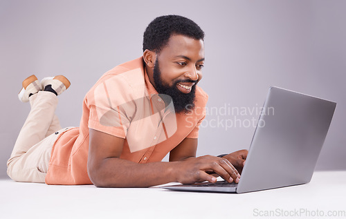 Image of Happy black man, laptop and studio floor to search social media, online shopping or subscription download. Smile, male model and computer technology for internet, typing email or elearning on website