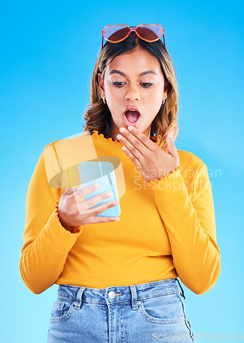 Image of Notification, shocked and woman surprised by phone due to trending social media news isolated in a studio blue background. Wow, omg and young female amazed by a cellphone using internet or online