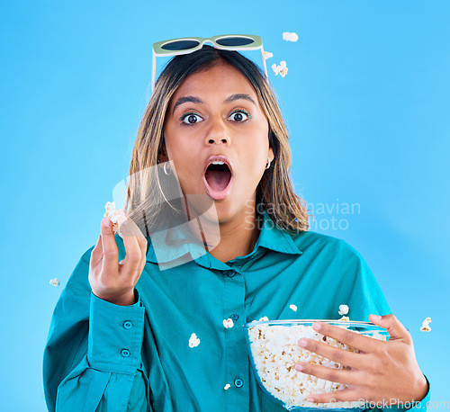 Image of 3D glasses, popcorn and wow with a woman in studio on a blue background looking shocked while eating a snack. Portrait, movie and video entertainment with an attractive young female feeling surprised