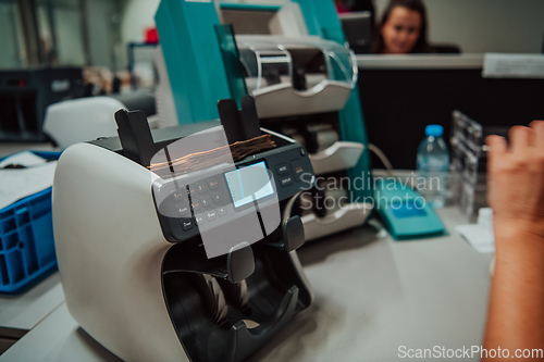 Image of Bank employees using money counting machine while sorting and counting paper banknotes inside bank vault. Large amounts of money in the bank