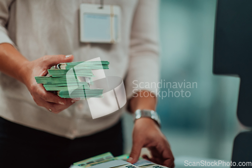 Image of Bank employees using money counting machine while sorting and counting paper banknotes inside bank vault. Large amounts of money in the bank