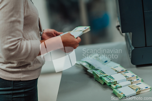 Image of Bank employees using money counting machine while sorting and counting paper banknotes inside bank vault. Large amounts of money in the bank