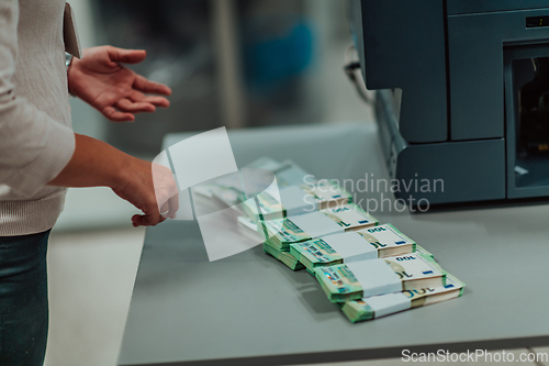 Image of Bank employees using money counting machine while sorting and counting paper banknotes inside bank vault. Large amounts of money in the bank