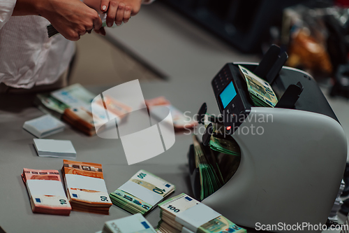 Image of Bank employees using money counting machine while sorting and counting paper banknotes inside bank vault. Large amounts of money in the bank