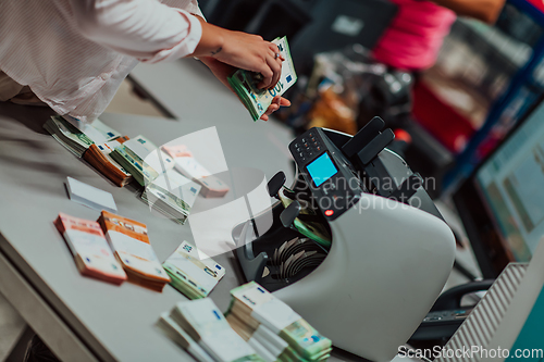 Image of Bank employees using money counting machine while sorting and counting paper banknotes inside bank vault. Large amounts of money in the bank