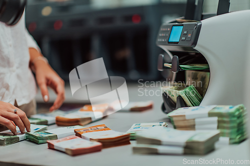 Image of Bank employees using money counting machine while sorting and counting paper banknotes inside bank vault. Large amounts of money in the bank